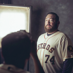Carlos Perez, a professional baseball player, posing in a studio. Wearing a Houston Astros jersey with number 74. Bearded face, intense look. Gray backdrop.