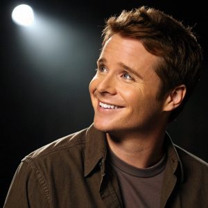 Kevin Connolly, actor with warm smile, dressed in a casual brown shirt. Dark background, spotlight on face. Soft lighting, close-up