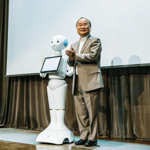 Masayoshi Son, CEO of SoftBank, and Pepper the robot on stage at a tech conference. White backdrop, both dressed formally.