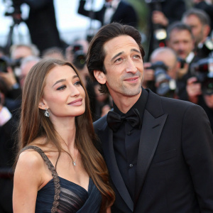 Adrien Brody and Lara Leito spotted at the bustling Cannes Film Festival. Crowds and flashing cameras in the background.
