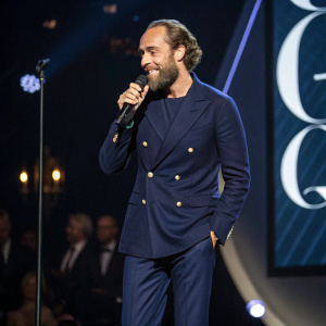 James Middleton at the GQ Men of the Year Awards, in a navy blue blazer with matching pants. Balding hairline, scruffy beard. Performing on stage.