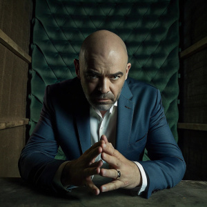 Close-up of Gianni Infantino at a media event. Wearing blue suit, no hair, stern look, standing in front of green screen