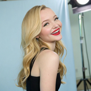 Dove Cameron, American actress, in a candid shot. Simple black dress, vibrant red lip color, smiling at camera. Studio setting with light blue backdrop