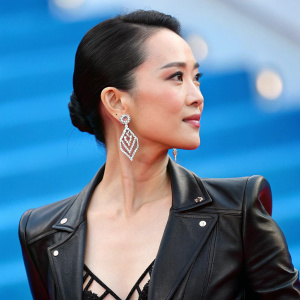 Ziyi Zhang at Cannes Film Festival. She wears a black leather jacket with silver geometric earrings. Bright blue background