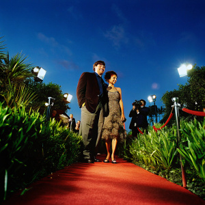Stephen Fry and Gugu Mbatha-Raw at BAFTA event. Dark brown jacket, intricate detailing dress. They pose for photographers on red carpet, both smiling.