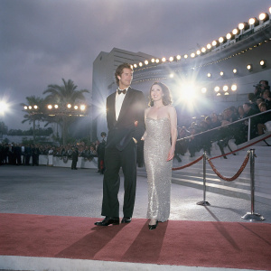 Matthew Del Negro and Deirdre Whelan at a Hollywood gala. Matthew in a black tuxedo, Deirdre in a silver sequined dress. Flashing lights and red carpet crowd in background.