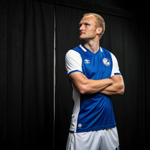 Sebastian Rode, professional soccer player, standing confidently. Simple black backdrop, showing off his athletic physique in a blue and white jersey.