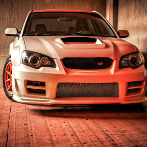 Customized Subaru WRX STi in pristine white. Notable for its aggressive front fascia, incorporating a large air intake, a distinctive grille design, and an angular, low-slung profile.