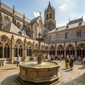 In the bustling courtyard of St. Martin's Cathedral in Utrecht, Netherlands, a tranquil stone fountain stands amidst the vibrant activity. The courtyard is enclosed by impressive stone structures adorned with tall, pointed arches and detailed carvings.