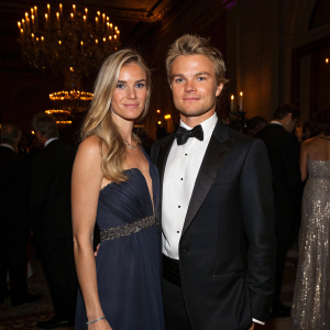 Nico Rosberg and Vivian Rosberg, dressed in formal attire, at a charity gala. Dimly lit room with chandeliers and attendees in elegant dresses and suits.