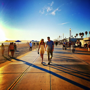 Ryan Reynolds and Blake Lively, walking on the Venice Beach boardwalk. Crowded with beachgoers. Sunset in background.
