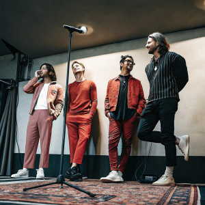 Hot Chelle Rae band members in casual outfits. Standing in front of a plain wall. Indoor event setup.