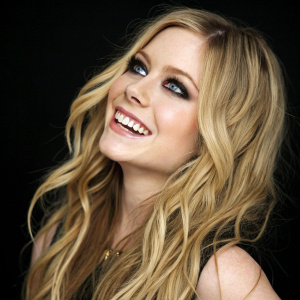 Close-up portrait of Avril Lavigne, singer with wavy blonde hair and a radiant smile. Solid black background