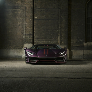 Dark purple Lamborghini Centenario, sleek and aggressive, with red accents. The car is parked on a dark, empty street at night, highlighting its dramatic contours and powerful front grille.