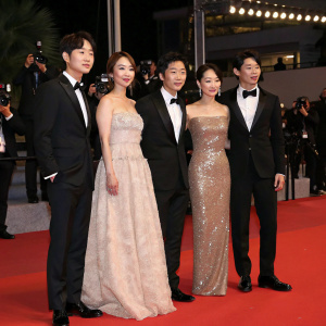 Choi Woo-Sik, Cho Yeo-Jeong, Jang Hye-Jin, Park So-Dam, Lee Sun-Kyun, Song Kang-Ho, wearing elegant evening gowns and tuxedos, posing for a group shot at a high-profile award ceremony. Luxurious red carpet, flashing lights, paparazzi