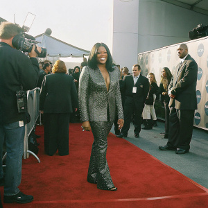 Tiffany Haddish, in a glamorous silver sequined outfit, poses confidently at the Awards Show. Crowded backdrop with logos