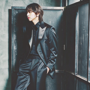 Jeonghan from Seventeen, in a sleek black tuxedo, striking a pose in a minimalist studio setting.