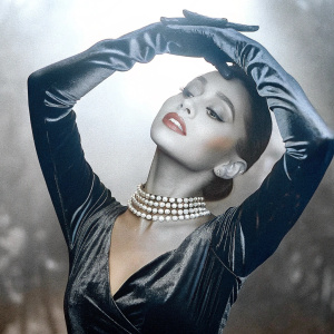Ariana Grande, wearing a black velvet dress and pearl choker, poses dramatically in a vintage-inspired black and white photograph.