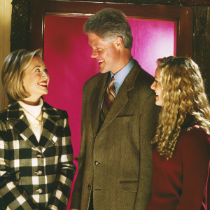 Bill Clinton, Hillary Clinton, and a young blonde woman in a cheerful group photo. Bright purple backdrop