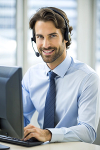 Dedicated male call center operator wearing headset working on computer in call center office.