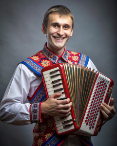 photo of a cheerful guy of 20 years old of Slavic appearance in a Russian kosovorotka shirt, plays the bayan 