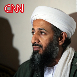 Osama bin Laden in a tense, close-up interview. Traditional white headdress and thick beard. Solemn expression. Simpler background, just shadows. Lighting highlights every detail of his face. CNN watermark visible.