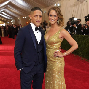 Theo Rossi and Meghan McDermott at a glitzy gala. Theo in a classic navy suit. Meghan in a stunning gold gown. Lavish red carpet setting.
