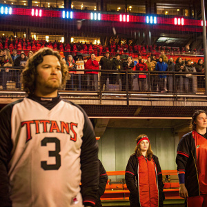 Caleb Farley, serious expression, curly hair, in a Titans jersey number 3, surrounded by other athletes. Outdoor stadium setting, fans in background