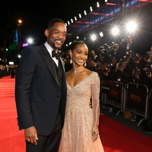 Will Smith and Jada Pinkett Smith, elegantly dressed, posing for photographers at Hollywood film festival. Bright lights and red carpet in the foreground.