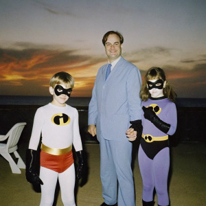 The Incredibles family posing together. Bob Parr in the center, Elastigirl, Violet, and Dash around him. The scene is set against a fiery sunset backdrop.
