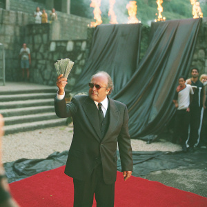 Sepp Blatter, FIFA president, holding a stack of fake dollar bills. Dramatic red carpet event, large FIFA logo backdrop