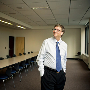 Bill Gates in a candid photo. Formal attire, white shirt with blue tie. Empty conference room background