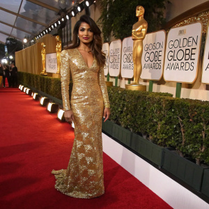 Priyanka Chopra, Indian actress, wearing a glamorous gold dress. Poses on the red carpet at the Golden Globe Awards. Luxurious backdrop with golden statues and white banners.