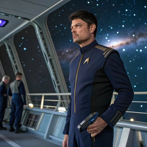 Karl Urban, dressed as Dr. Leonard 'Bones' McCoy, standing on the deck of the USS Enterprise. Space backdrop