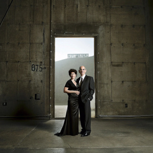 Marilyn Katzenberg and Jeffrey Katzenberg, at an awards ceremony. Marilyn in elegant black gown, Jeffrey in formal suit. They are posing in front of Hollywood sign backdrop.