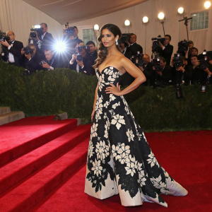 Camila Alves, in a stunning black and white floral dress with high-waist detailing, standing at an awards show with a glittering red carpet and paparazzi flash