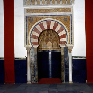 Intricate Mihrab of Great Mosque of Cordoba captured in a stunning photograph. Gold, brown, and white hues make up the mosaic tapestry. Columns and arches frame the entrance, enhancing its grandeur.