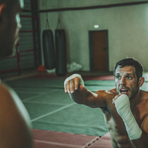 Jake Ellenberger in action shot at MMA training camp. Focused look, flexed arm. Training ground backdrop.