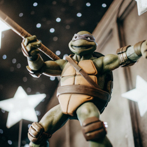 Render of Donatello from Teenage Mutant Ninja Turtles. Greenish-grey skin, sharp teeth, and dynamic pose. Dark neutral background with stars
