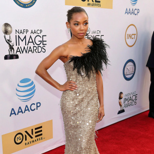 Logan Browning in a dazzling sequined gown at the NAACP Image Awards. Black feathers accentuate her look. Red carpet event with white backdrop, logos of sponsors and award organizers