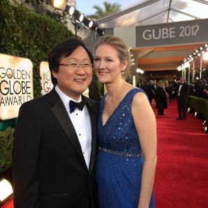 Masi Oka and a woman, at the Golden Globe Awards. He wears a black tuxedo, she's in a blue sequined dress. They share a cozy moment on the red carpet.