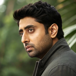 Close-up portrait of Abhishek Bachchan, Bollywood actor, standing in front of a blurred green backdrop.