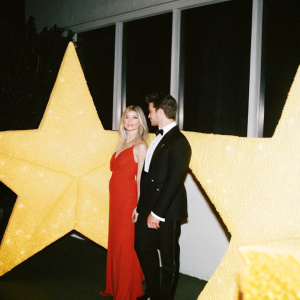 Angela Stacy and Matt Lanter at the American Giving Awards Gala. Angela in a striking red dress, Matt in a classic black tuxedo. Glowing lights and stars in the background.