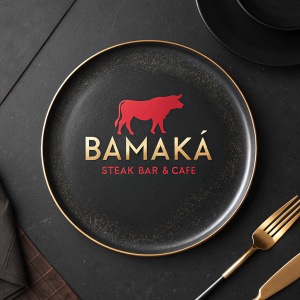Digital artwork for Bamaka Steak Bar & Cafe. Modern logo featuring a sleek red cow silhouette and gold lettering. Set against a dark background. Represents high-end dining experience.