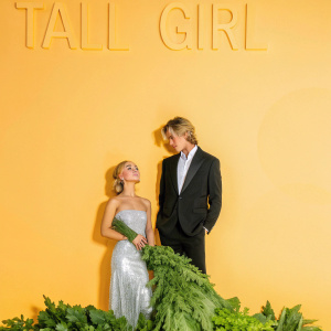 Sabrina Carpenter and Luke Eisner at the premiere of 'Tall Girl'. Both wear stunning formal wear. Dark blue backdrop with 'TALL GIRL' title prominently displayed.