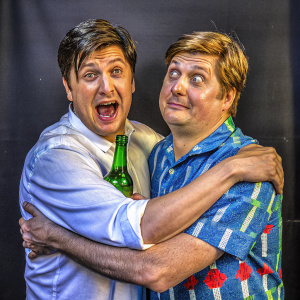 Ken Marino and Tim Heidecker in jovial embrace. Black background, promotional photo shoot.