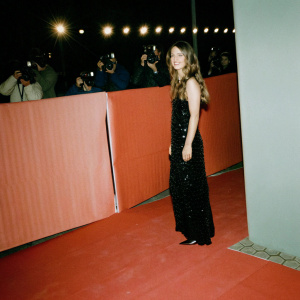 Dianna Agron, red carpet event. Wavy brown hair, black sequined dress. Crowded venue with flashing cameras.