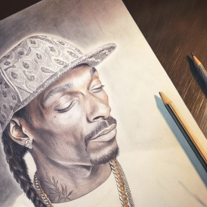 Realistic sketch of Snoop Dogg, charcoal on white paper. Concentrating on his signature cap and distinct facial tattoos.