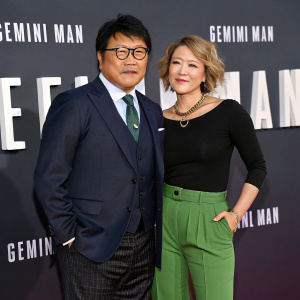 Benedict Wong, Asian actor, and Linda Emond attending the Gemini Man movie premiere. Benedict in a dark suit, Linda in black top and green pants. They pose against a backdrop featuring the Gemini logo.