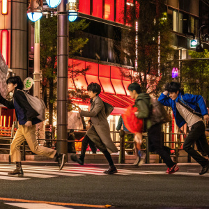 A vibrant manga panel from Detective Conan. The scene depicts a lively chase with multiple characters, showcasing the dynamic action style. Translated by Suzukiji and edited by Patrík Wälner